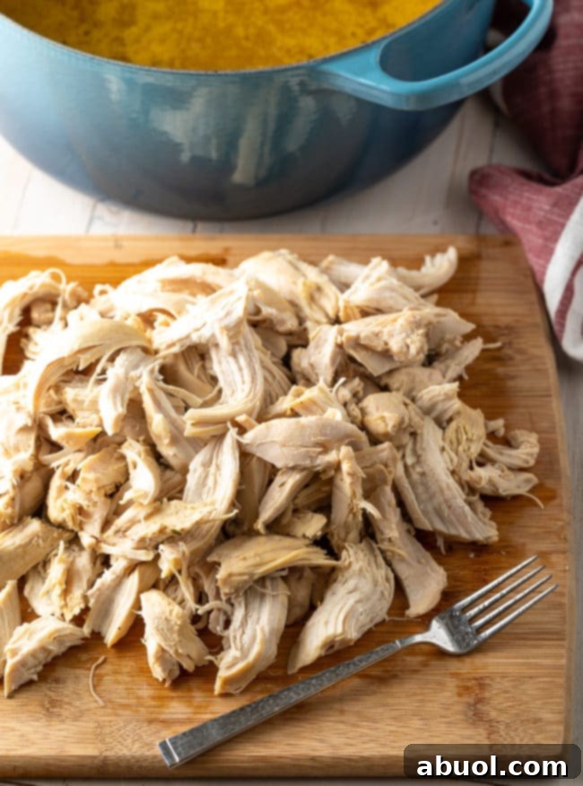 Tender pieces of shredded chicken, pulled off the bone and placed on a wooden cutting board, ready to be added back to the pot.