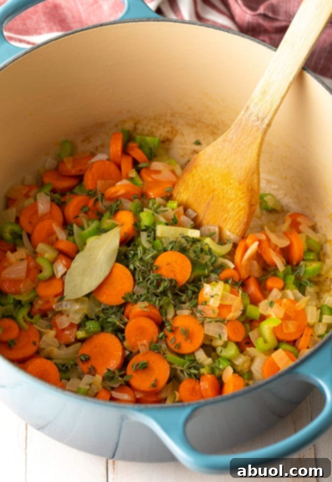 Diced onions, celery, and carrots sautéing in melted butter in a large soup pot with a wooden spoon.
