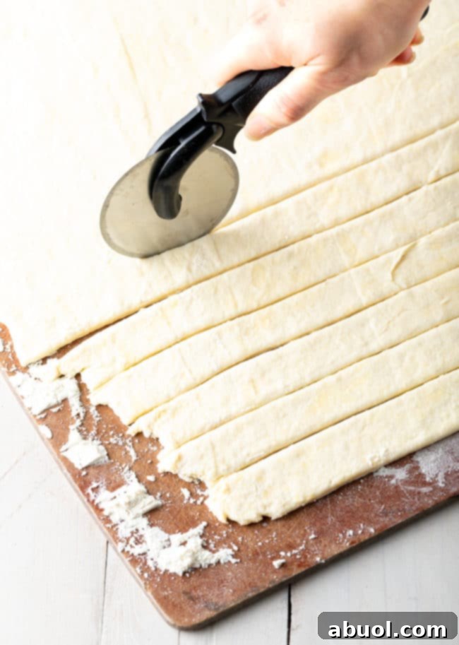 A pizza cutter efficiently slicing rolled dumpling dough into uniform strips on a cutting board.