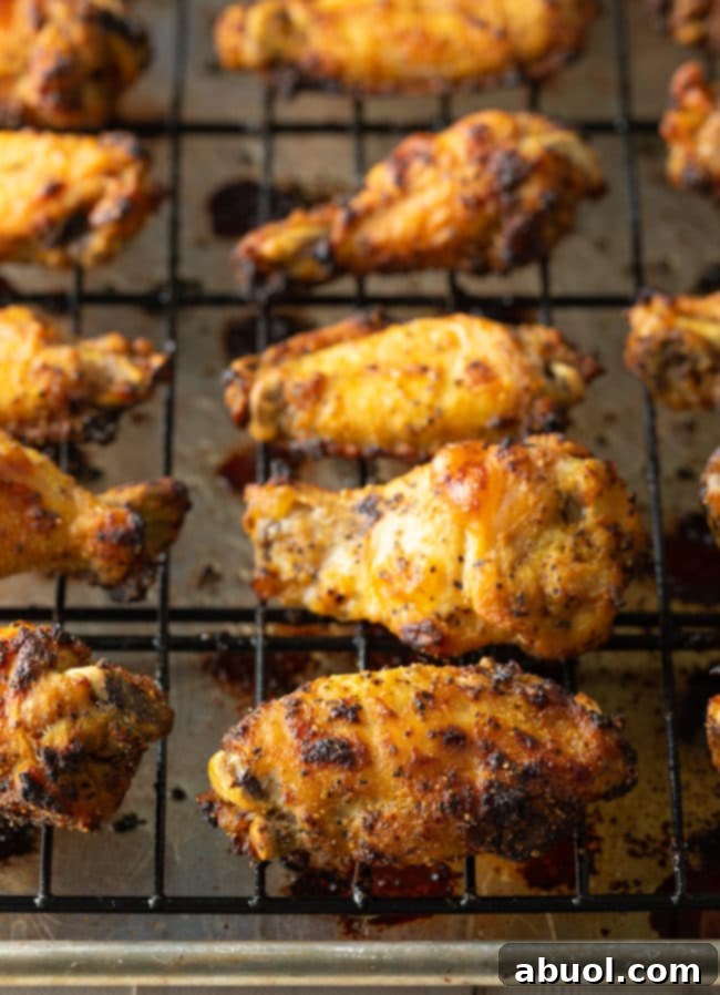 Crispy Baked Lemon Pepper Wings 4 Baked lemon pepper wings arranged on a wire rack over a baking sheet, ready for the oven.