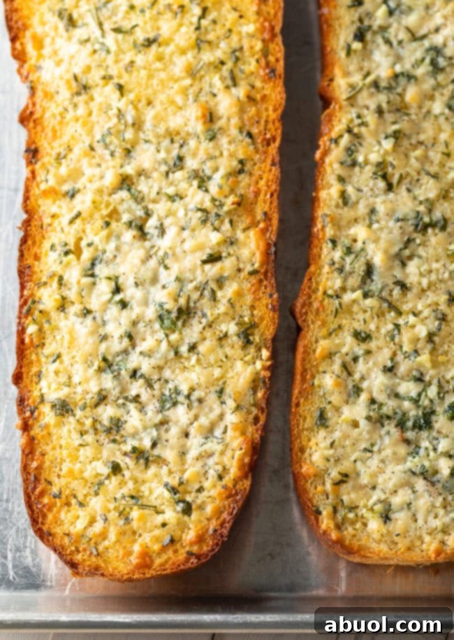 Top down view two loaves of crusty cheesy garlic bread with fresh herbs.