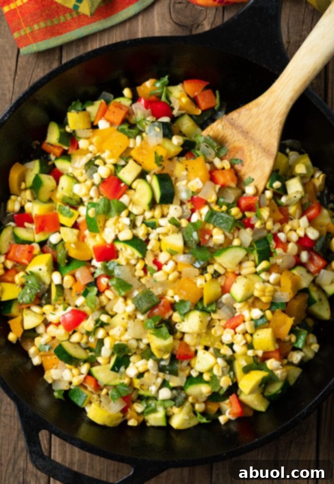 Mexican Calabacitas recipe in a large cast iron skillet with a wooden spoon. 