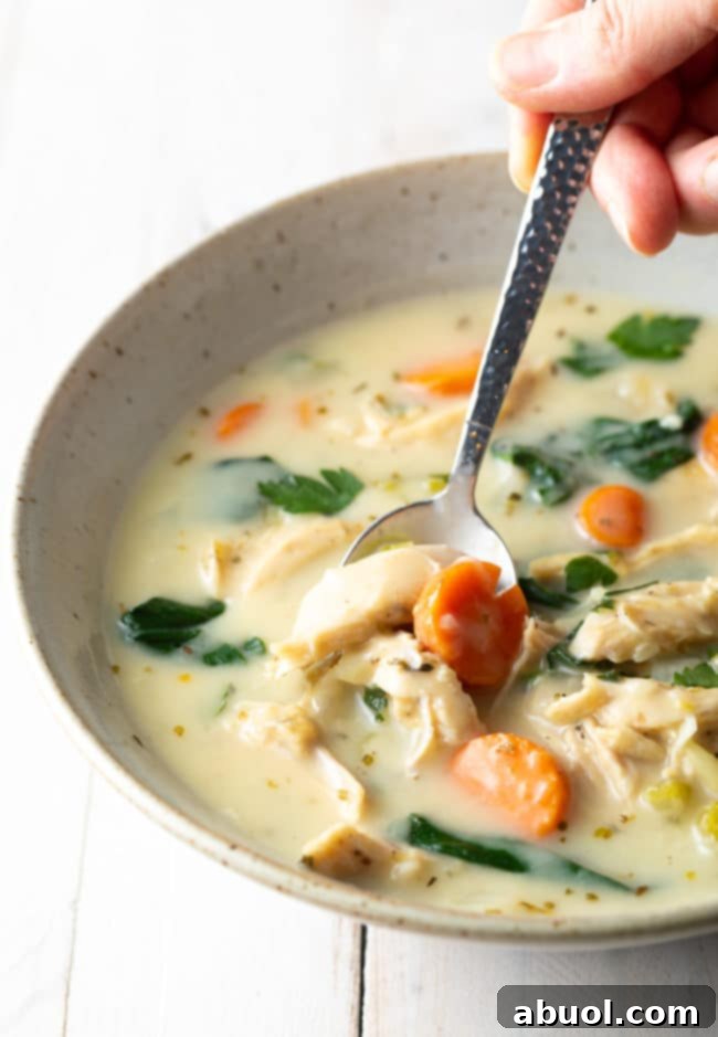 Velvety Lemon Chicken & Spinach Soup 11 Chicken soup in a bowl with a spoon scooping up a bite, showing the creamy texture and ingredients.