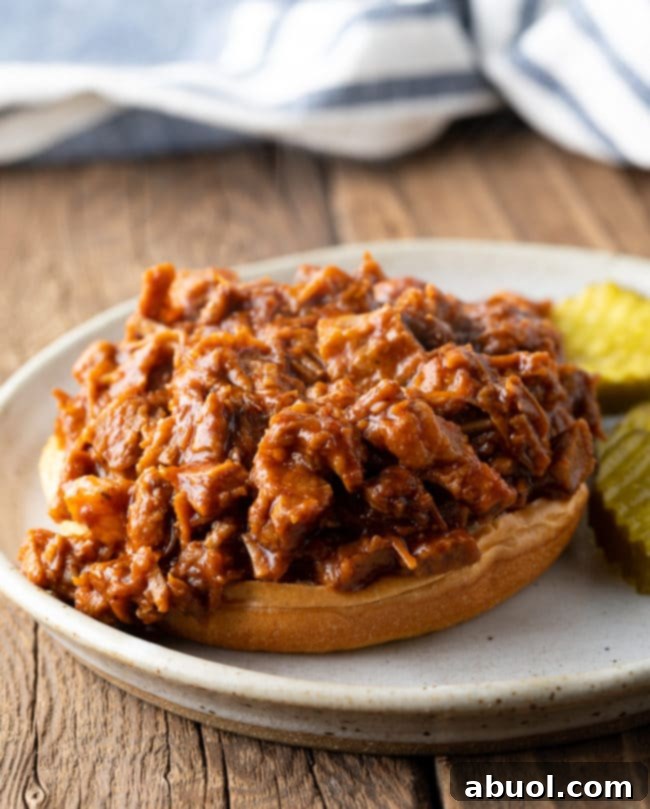 An open-faced chopped beef brisket sandwich on a bun, showcasing the tender meat and rich sauce.