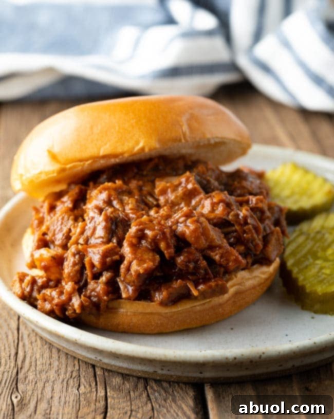 A delectable chopped beef brisket sandwich presented beautifully on a plate, accompanied by two crisp pickle spears.