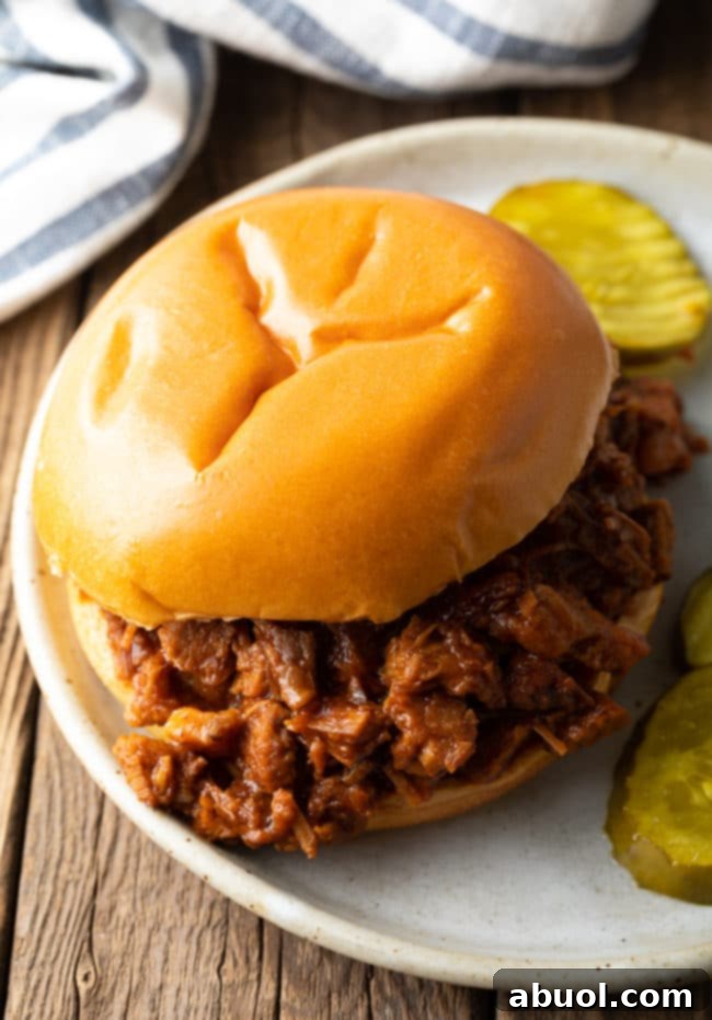 A delicious chopped beef brisket sandwich on a soft bun, garnished with sliced pickles, ready to be enjoyed.