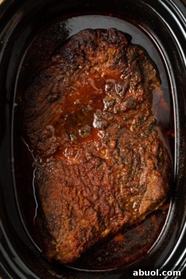Tender, cooked brisket resting in the slow cooker after hours of slow cooking.