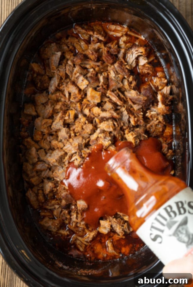 Adding rich BBQ sauce to finely chopped beef brisket in the slow cooker, preparing for the final simmer.
