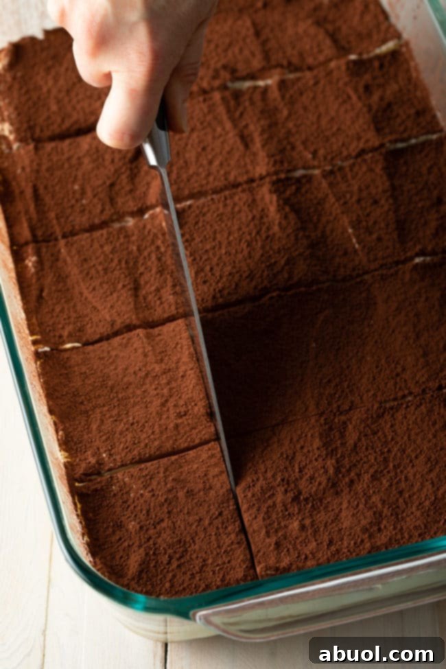 A hand uses a sharp knife to meticulously cut the easy tiramisu into perfect squares, ready for serving.