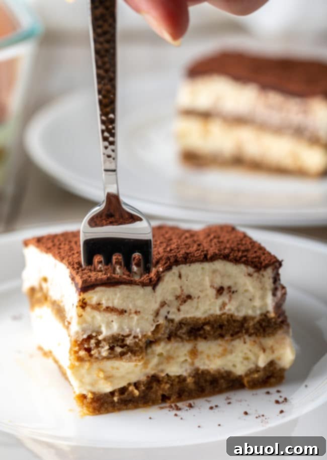 A delicious slice of easy Tiramisu cake on a plate, with a fork poised to take a bite, highlighting its rich layers.