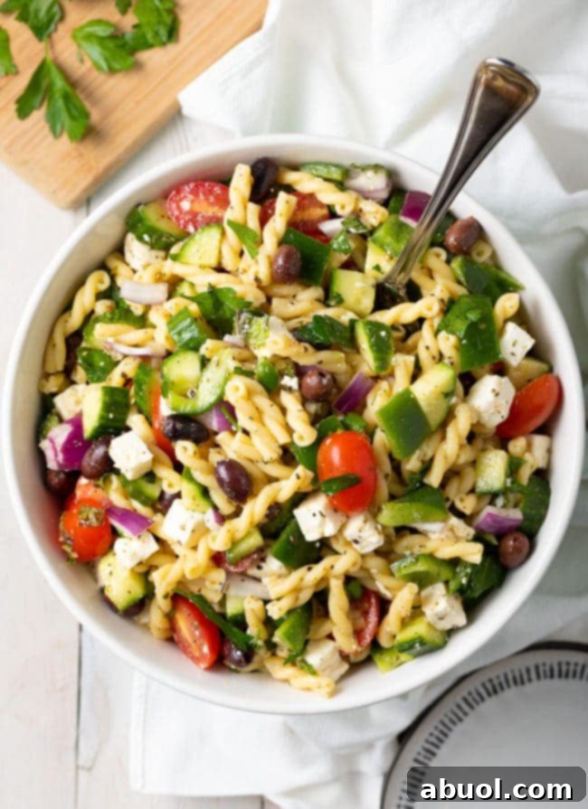 Greek Pasta Salad Recipe in a bowl with spoon, showcasing colorful vegetables and feta
