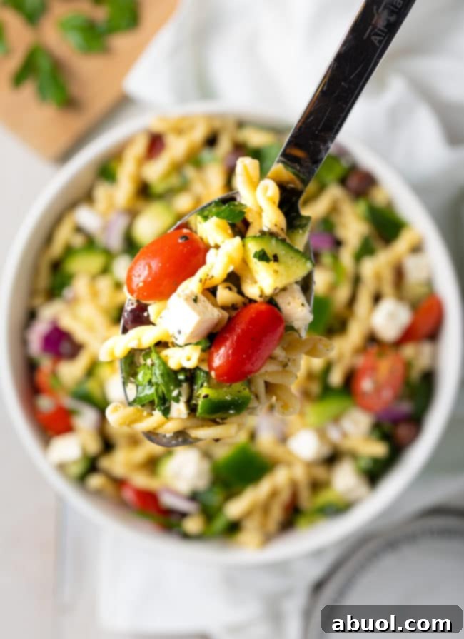 Pasta Salad Recipe lifted on spoon over a bowl, highlighting the vibrant ingredients