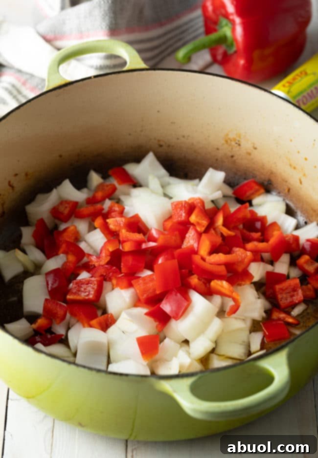 Authentic Cuban Arroz Con Pollo 7 Chopped onion and red bell peppers being sautéed in a dutch oven.