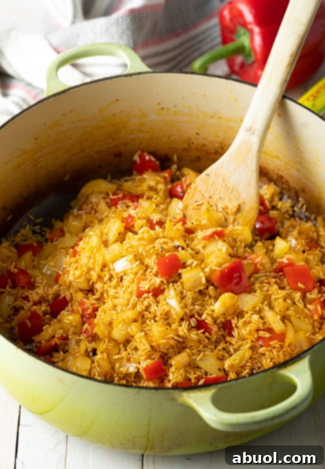 Authentic Cuban Arroz Con Pollo 8 Long-grain rice being mixed and sautéed with onions and bell peppers in a dutch oven.