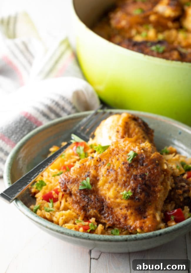 Authentic Cuban Arroz Con Pollo 10 A serving of Cuban Chicken and Rice in a blue bowl with a silver fork, garnished with fresh cilantro.