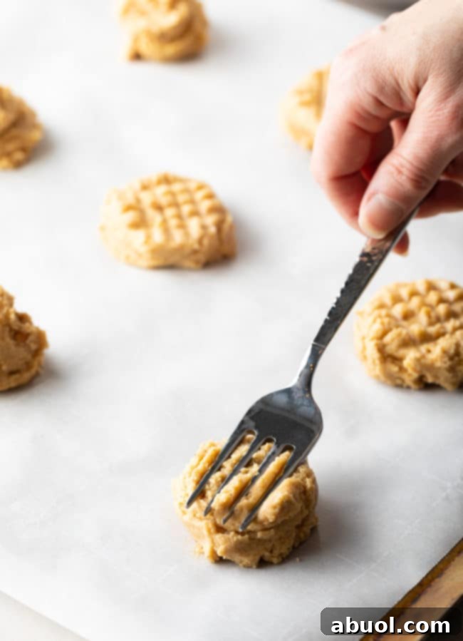 Pressing Best Peanut Butter Cookie Recipe dough balls with a fork to create the classic criss-cross pattern.