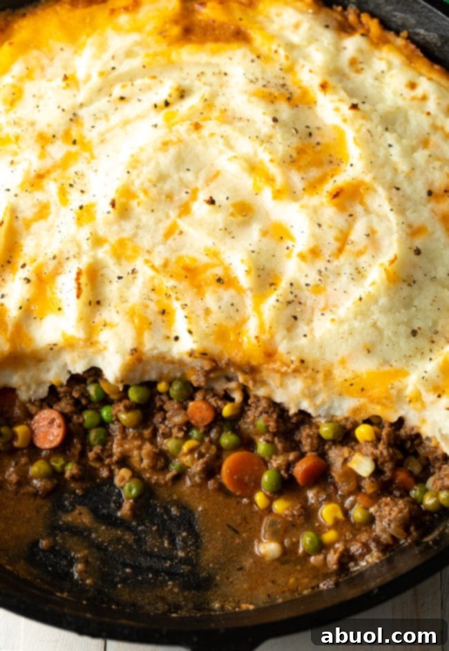 A perfectly baked golden-brown Cottage Pie with a portion removed, revealing the rich, savory beef and vegetable filling beneath a fluffy mashed potato topping.
