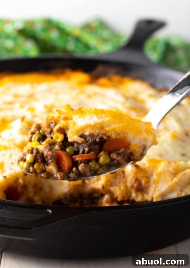 A generous serving of Shepherd's Pie being spooned out of a deep pan, showcasing the golden-brown mashed potato crust and the hearty filling underneath.
