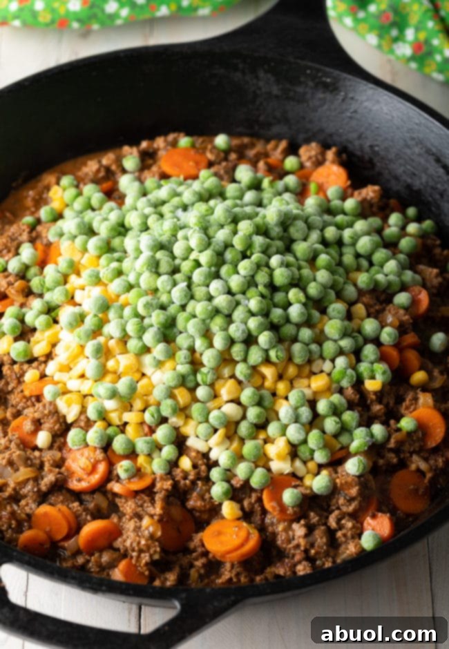 A cast iron skillet filled with the vibrant and chunky Cottage Pie filling, actively cooking on a stovetop, before being topped with mashed potatoes.