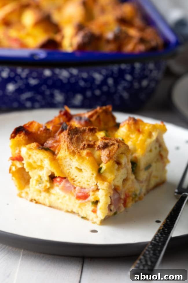 Slice of egg strata on a plate, showing fluffy layers with ham, cheese, and roasted red peppers