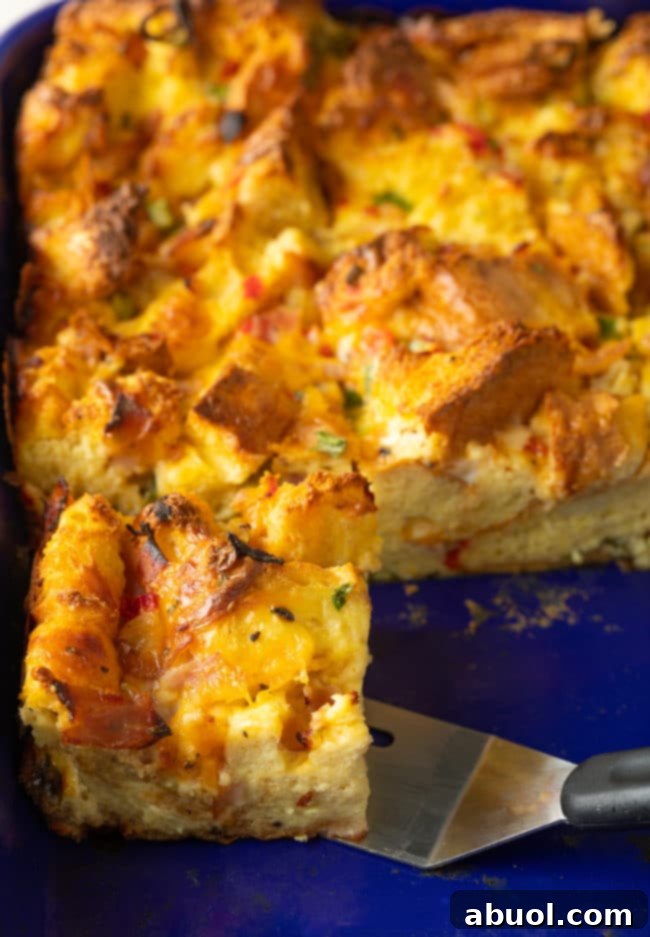 Fluffy strata recipe, a slice cut in the pan, revealing layers of eggs, bread, cheese, and ham