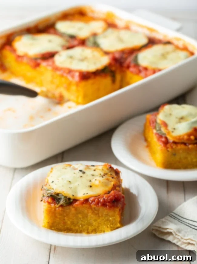 Baking dish of polenta topped with marinara sauce, basil, and sliced mozzarella cheese. A square of baked margherita polenta is on a white dish at the forefront.