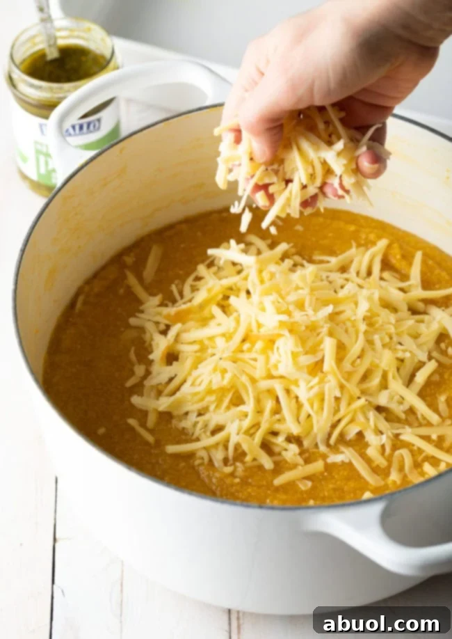 Adding shredded gouda cheese to a pot of soft polenta.