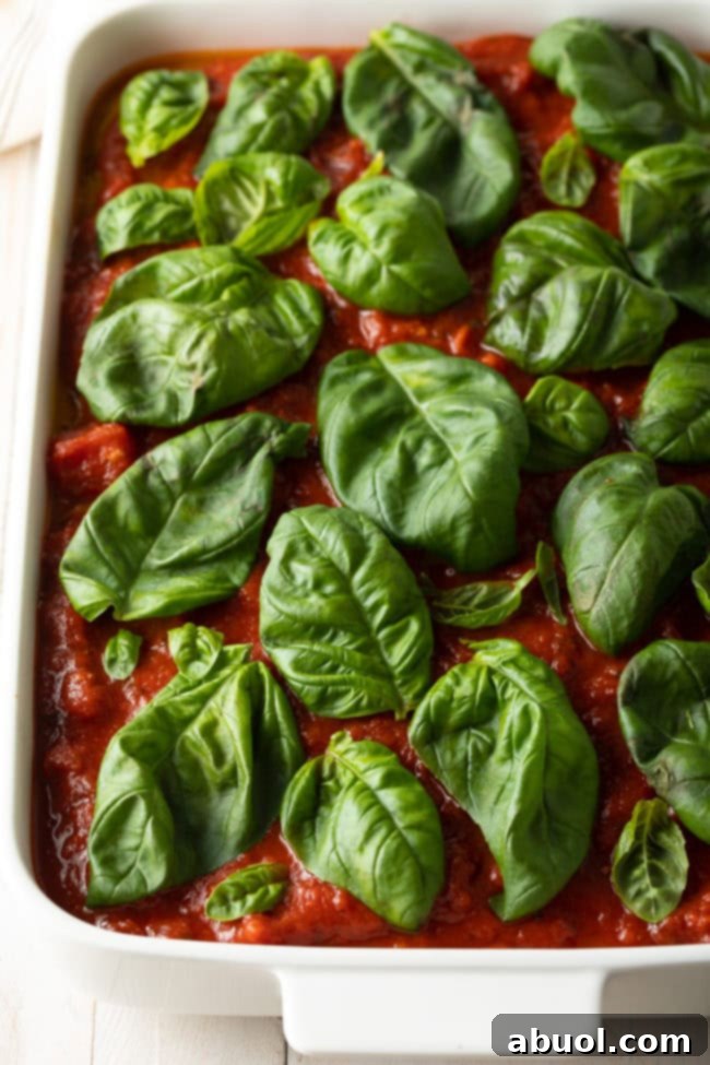White baking dish with marinara sauce, topped by fresh basil leaves.