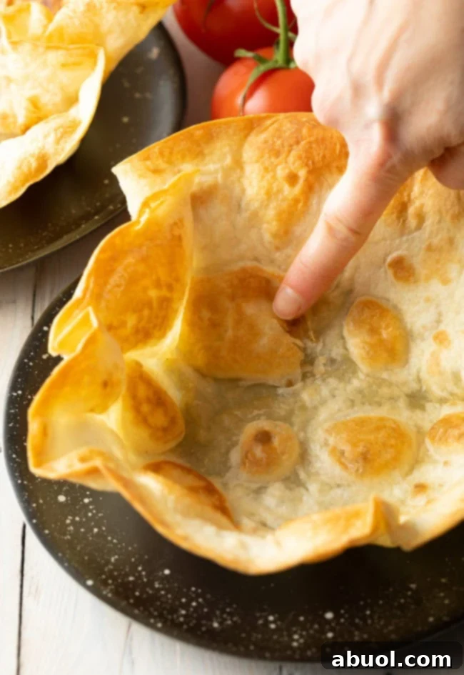 A crispy taco bowl shell on a plate, with a hand gently poking it to demonstrate its perfect crunch and bubbly texture.