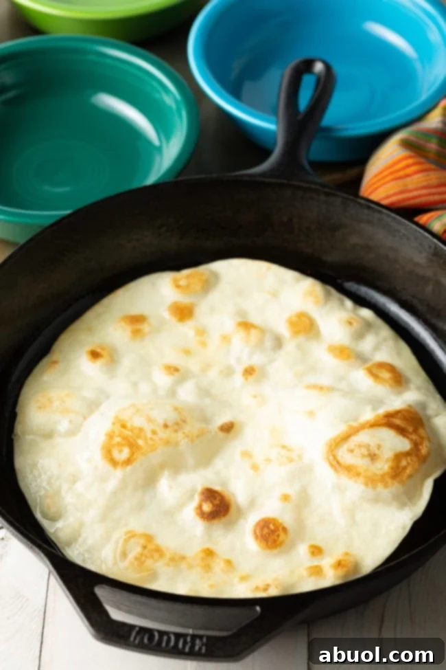 A flour tortilla frying in a pan, actively bubbling and puffing up as it cooks.