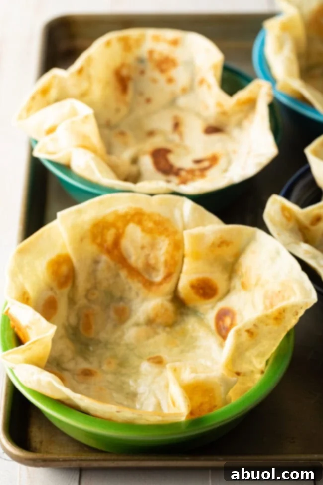 A freshly pan-fried tortilla, golden and bubbly, being gently placed into an oven-safe bowl for shaping.