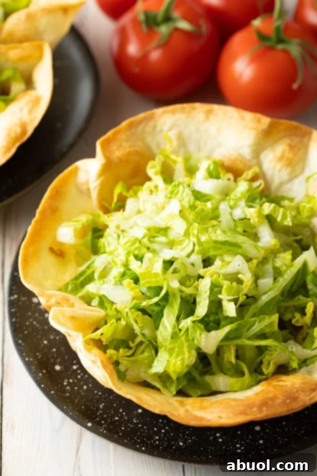 A perfectly shaped, crispy taco bowl shell, ready to be filled, with some shredded lettuce already added.