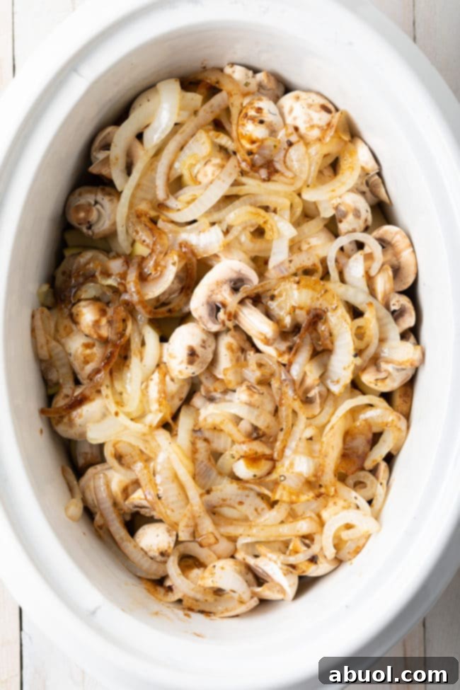 Potatoes, mushrooms, and onions prepared and layered in the slow cooker for brisket