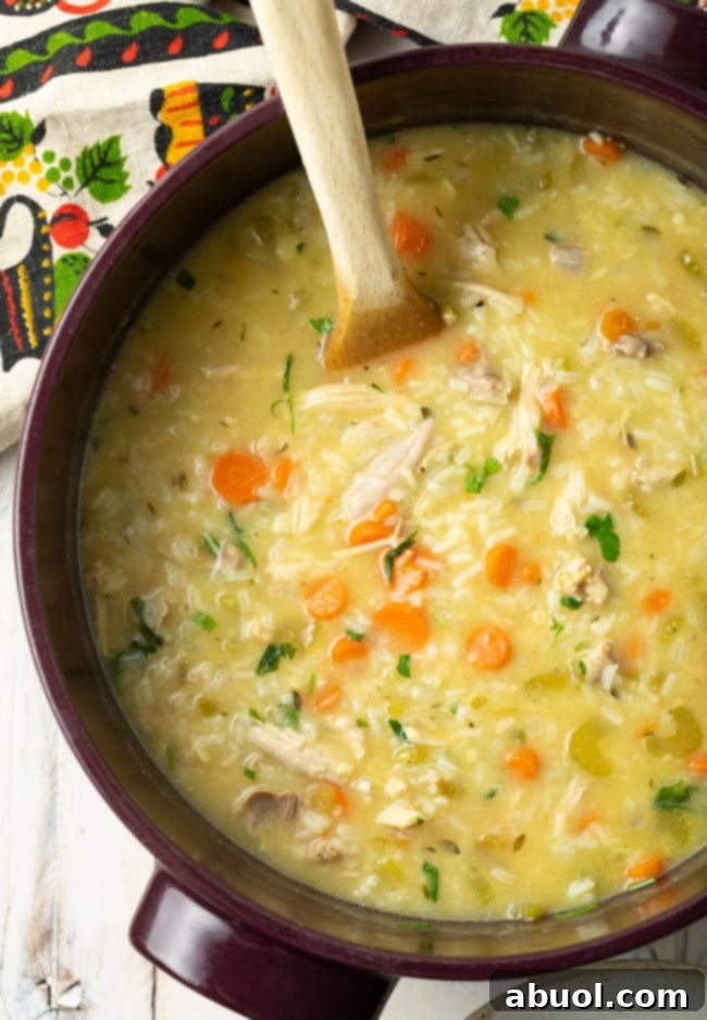 A large pot filled with creamy chicken and rice soup, ready to be served. A wooden spoon rests in the pot, inviting a taste of its rich texture.