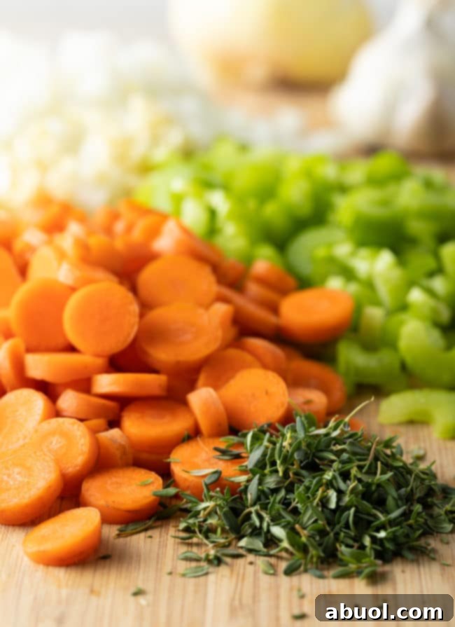 Freshly chopped onions, carrots, and celery are neatly arranged on a wooden cutting board, ready for the soup pot.