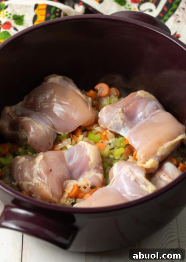 Raw chicken pieces and sautéed vegetables simmering gently in a large soup pot, promising a flavorful base for the creamy chicken and rice soup.