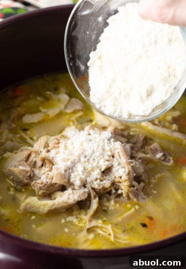 A hand gently pouring a mixture of cornstarch and grated Parmesan cheese into the simmering pot of chicken and rice soup, enhancing its creamy texture.