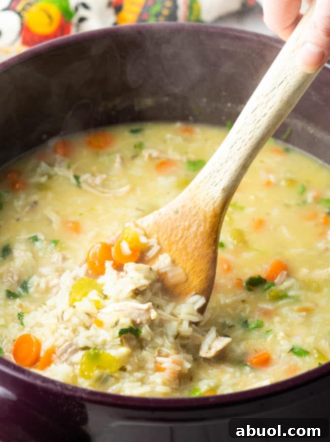 A wooden spoon stirring a rich, creamy chicken and rice soup in a large metal soup pot, showcasing the integrated ingredients and smooth consistency.