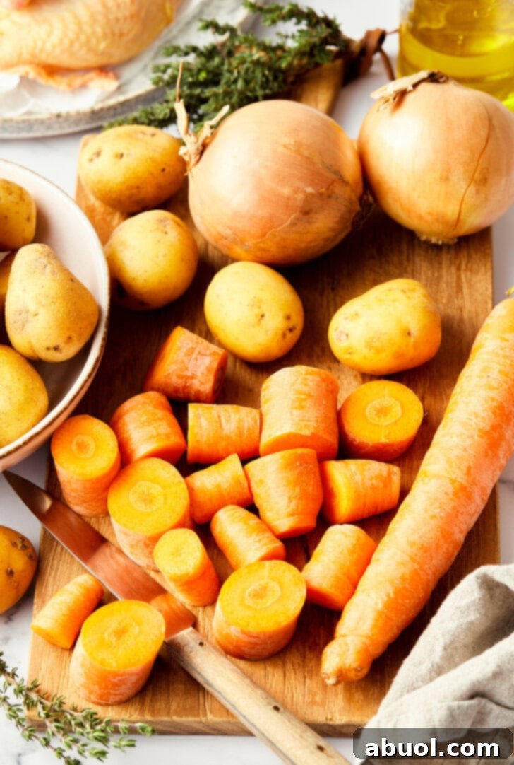 Various fresh ingredients laid out on a countertop, including Cornish hens, potatoes, carrots, onions, herbs, and butter, ready for making roasted game hens.