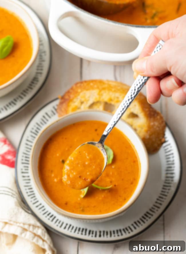 Roasted Tomato and Basil Velvet 11 Bowl of tomato soup with a hand holding a spoonful of soup above the bowl.