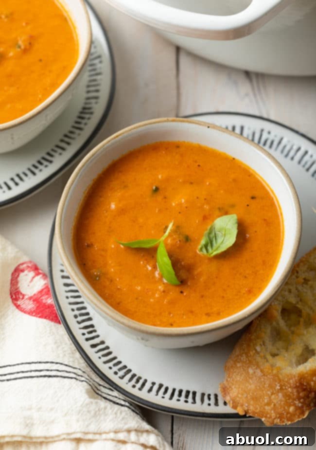 Roasted Tomato and Basil Velvet 4 Roasted tomato soup in a bowl with basil sprigs on top and a piece of bread on the side.