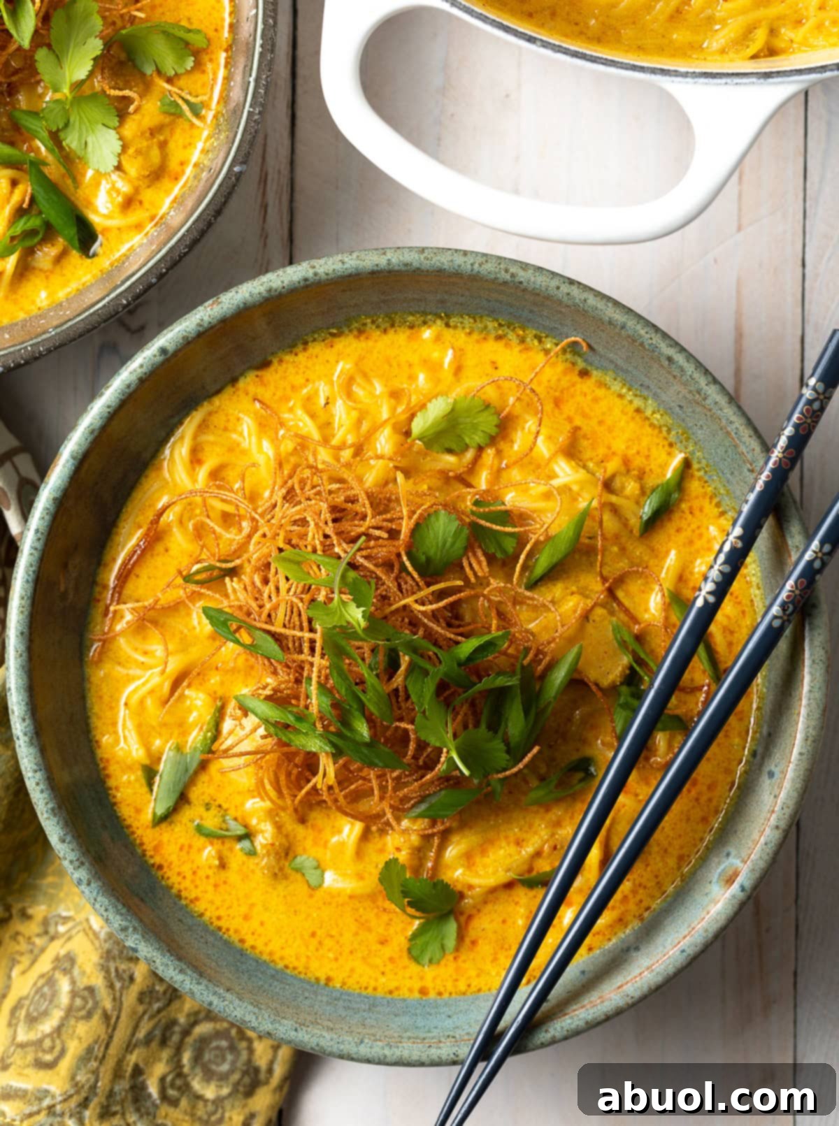 A top-down view of a steaming bowl of authentic Thai Khao Soi, garnished with fresh herbs and crispy fried noodles. Chopsticks rest on the bowl's rim, inviting you to dive into this rich coconut curry soup.