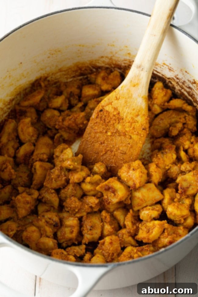 Sautéing chicken pieces in the fragrant coconut curry paste, an essential step for flavor.
