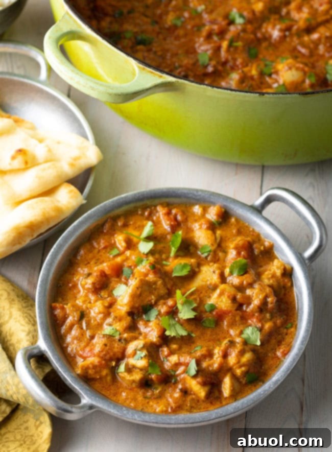 Fiery South Indian Chicken Curry 11 Easy Chicken Madras Curry in a silver bowl next to naan bread and a dutch oven.