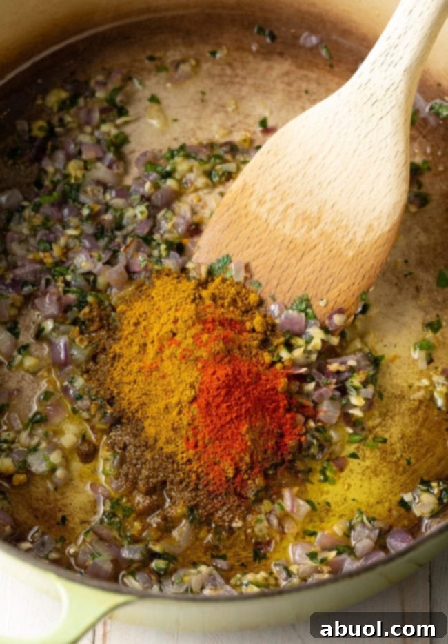 Fiery South Indian Chicken Curry 6 Spices and aromatics in a dutch oven being sautéed and stirred with a wooden spoon.