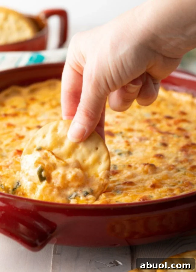 A hand expertly scooping a generous portion of hot shrimp dip onto a cracker, highlighting the dip's creamy, irresistible texture.