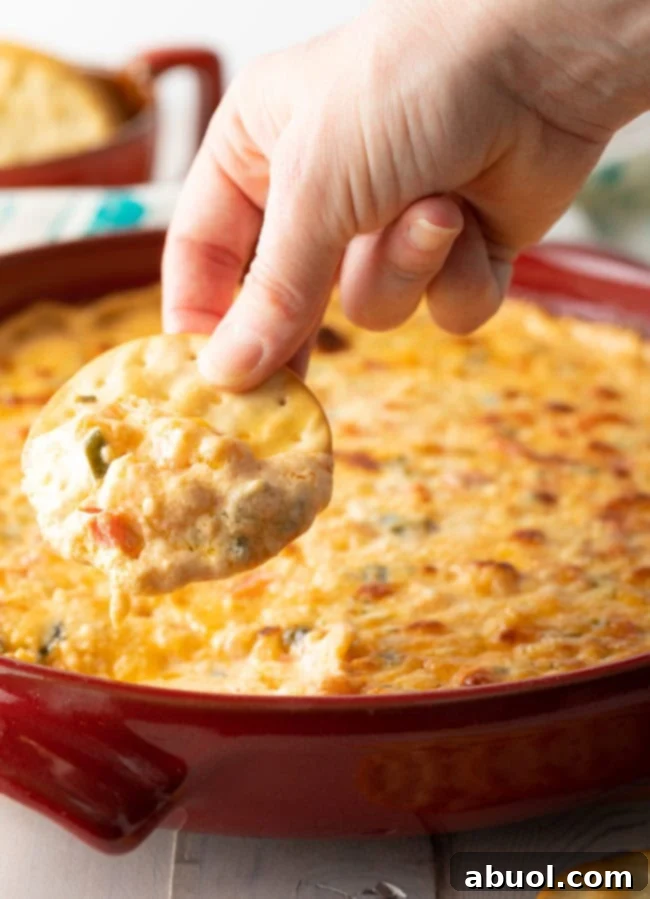 A hand holding a crunchy cracker, freshly dipped into the rich, hot shrimp dip, steam gently rising.