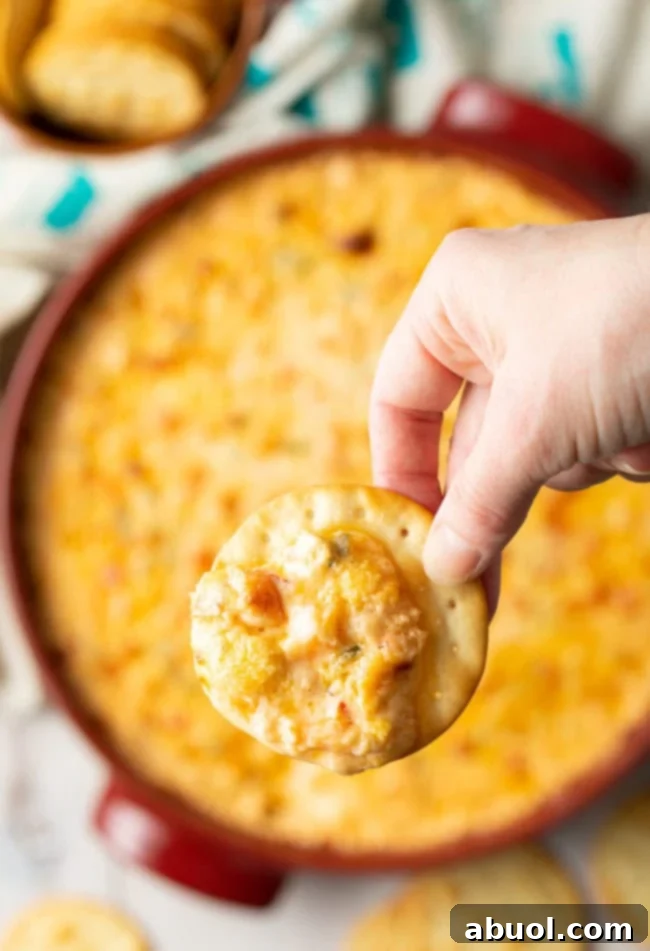 A cracker, generously loaded with the hot Cajun shrimp dip, is held in a hand, ready to be enjoyed.