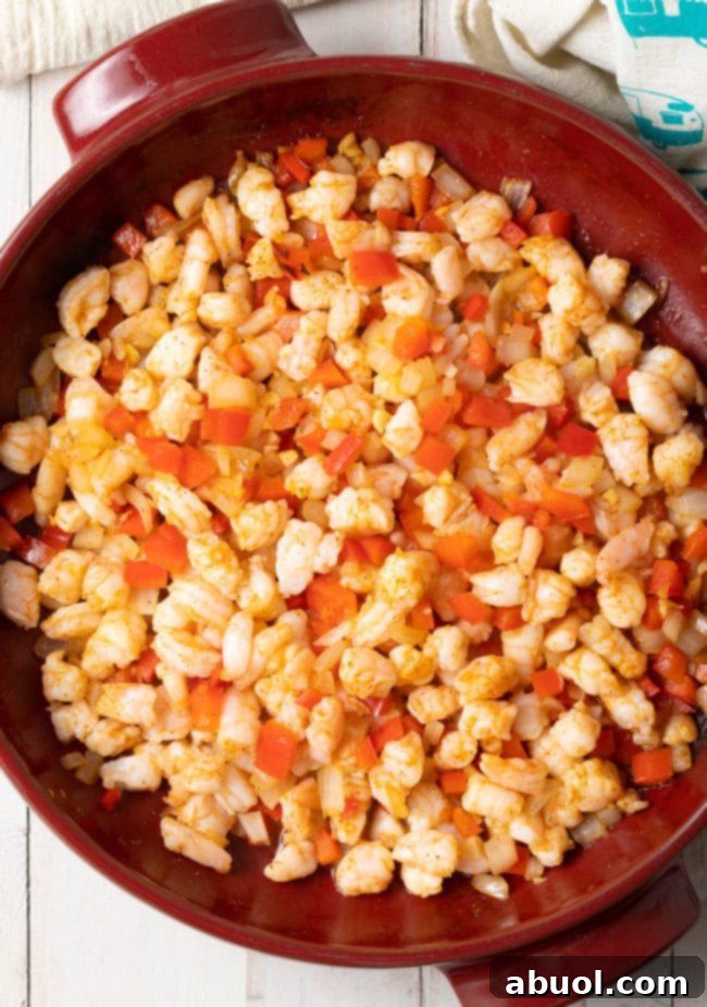 The hot shrimp dip, a mixture of shrimp, cheeses, and vegetables, is mixed together in a baking dish, ready for the oven.