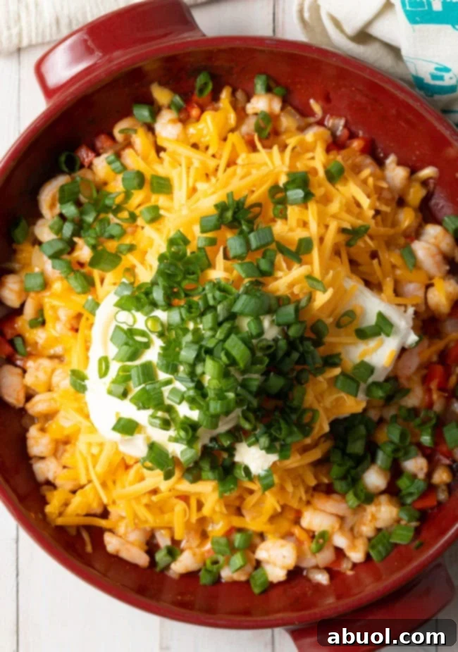 A generous layer of shredded cheese being added over the mixed dip ingredients in a baking dish, prior to baking.